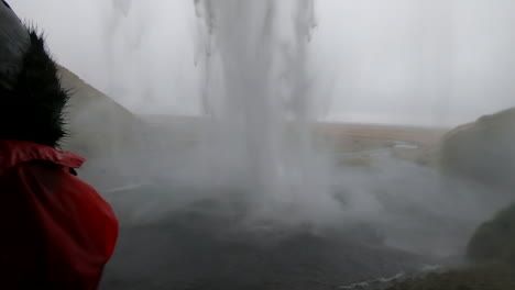 Schöne-Aufnahme-Hinter-Dem-Isländischen-Wasserfall-Seljalandsfoss-Und-Wo-Eine-Frau-Die-Schönheit-Und-Stärke-Des-Fallenden-Wassers-Bewundert
