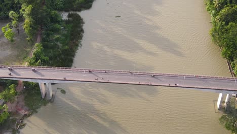 Muddy-water-of-river-with-bridge-leading-over-with-traffic,-aerial-view