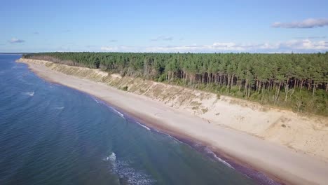 Aerial-view-of-Baltic-sea-beach-at-Jurkalne-on-a-sunny-day,-white-sand-cliff-damaged-by-waves,-coastal-erosion,-climate-changes,-wide-angle-drone-shot-moving-forward-high-1