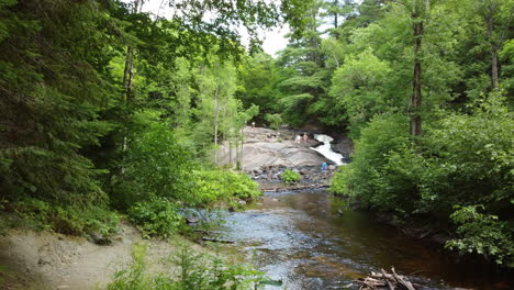 Aerial-drone-shot-of-the-Little-East-River-at-Stubb’s-Falls-as-a-group-of-people-relax-on-the-rocks-enjoying-a-beautiful-day-outdoors-at-Arrowhead-Park,-Ontario,-Canada
