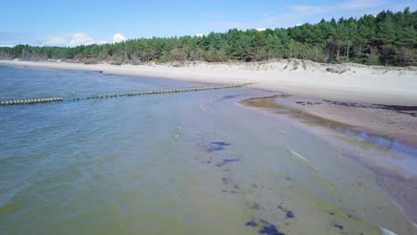 Aerial-panoramic-view-of-Baltic-sea-coast-on-a-sunny-day,-old-wooden-pier,-white-sand-dunes-damaged-by-waves,-coastal-erosion,-climate-changes,-wide-angle-drone-shot-moving-forward