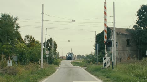 Ein-Blauer-Traktor-überquert-Mitten-Im-Grünen-Einen-Offenen-Bahnübergang