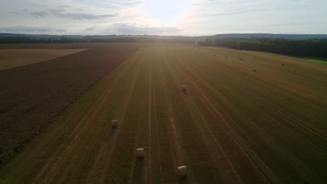 Aerial-drone-forward-moving-shot-of-sunlight-falling-on-golden-field-with-hay-bales-or-straw-bales-after-harvest