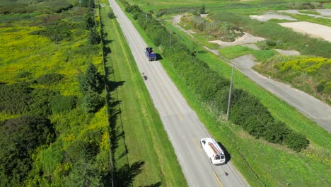 Aerial-of-cars-and-truck-driving-down-straight-rural-road-through-countryside