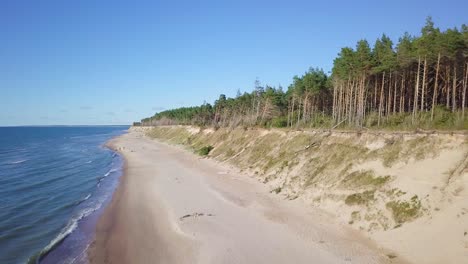 Aerial-view-of-Baltic-sea-beach-at-Jurkalne-on-a-sunny-day,-white-sand-cliff-damaged-by-waves,-coastal-erosion,-climate-changes,-wide-angle-ascending-drone-shot-moving-forward-1