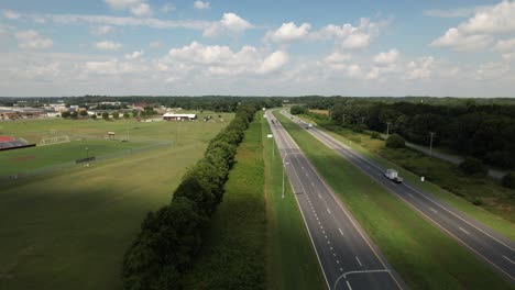 An-aerial-view-of-a-long-road-adjacent-to-a-green-field-with-a-line-of-trees-separating-them