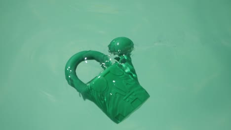Grüne-Plastikgießkanne,-Die-Auf-Der-Pooloberfläche-Schwimmt