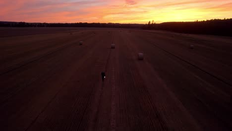 Aerial-drone-shot-of-golden-field-with-hay-bales-or-straw-bales-after-harvest-over-colorful-sky-after-sunset