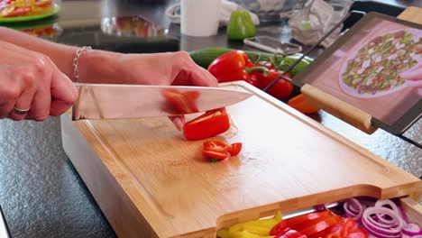 Close-up-of-a-wooden-cutting-board-while-a-red-bell-pepper-is-being-cut-with-other-vegetables-and-a-tray-with-recipe-on-the-board