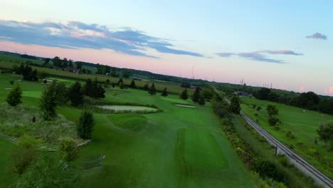 Frei-Fliegende-Luftaufnahme-Des-Grünen-Golfplatzes-Während-Des-Atemberaubenden-Sonnenuntergangs