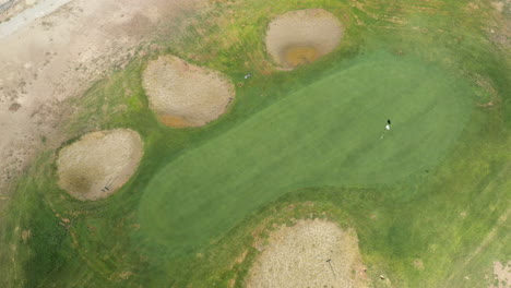 Golf-course-green-with-sand-traps---tilt-down-ascending-aerial-view