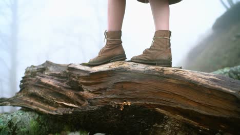 Close-up-of-woman-walking-over-a-fallen-tree-in-the-forest,-slow-motion-shoot