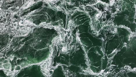 Churning,-swirling-white-water-below-a-surge-barrier-as-seen-from-above