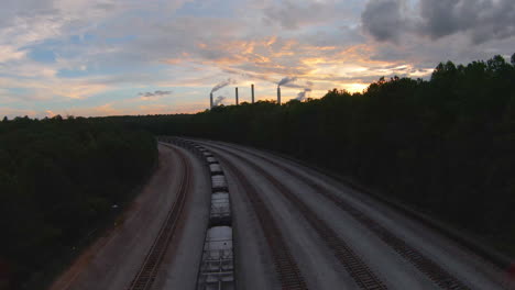 FPV-Flight-over-Rail-Road-Tracks-and-Forest-with-Power-Plant-in-Distance-during-Golden-Hour