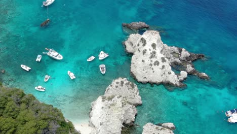 Multiple-boats-are-sailing-in-the-crystal-blue-as-seen-from-the-cliff-of-Tremiti-island-in-Italy,-and-a-drone-was-used-to-capture-the-beautiful-view