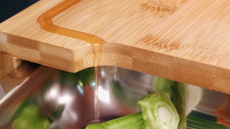 Close-up-of-a-juice-groove-with-flowing-juice-from-a-cutting-board-with-a-bowl-of-cut-vegetables-and-herbs-in-a-modern-kitchen