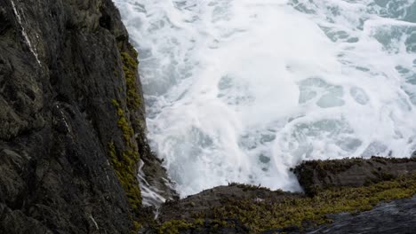 Foamy-Waves-Crashing-Into-Rocks-Covered-With-Moss-In-Newquay-Harbour,-Cornwall,-UK