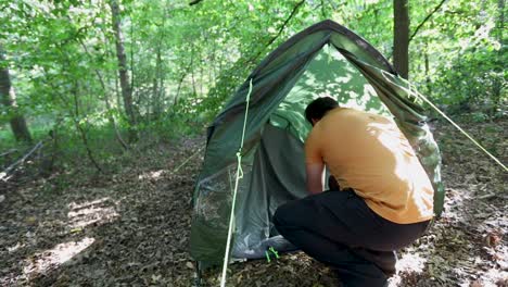 Young-adult-man-setting-up-tent-in-forest-campsite,-back-slow-motion-view