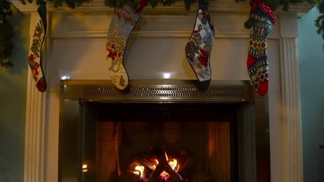 Tilt-down-motion-from-Christmas-socks-hanging-on-Fireplace,-Wood-burning-with-hot-flames,-Slow-motion