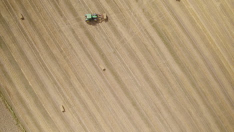 Aerial-top-down-of-tractor-collecting-hay-bales-of-farm-field-in-sunlight,4K
