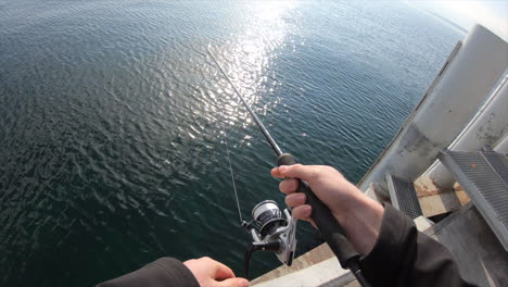 Pov:-a-fisherman-is-at-the-end-of-a-pontoon-in-a-Swiss-port-on-Lake-Geneva,-he-turns-his-reel-and-tries-to-catch-a-pike