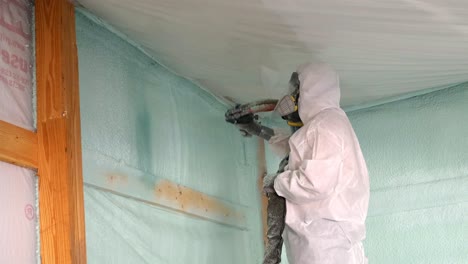 Worker-in-respirator-and-Tyvek-suit-sprays-closed-cell-foam-insulation-near-the-ceiling-of-a-newly-constructed-exterior-wall