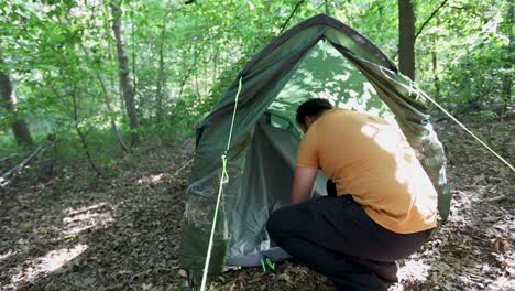 Young-man-trying-to-set-up-a-tent-in-woodland-campsite,-back-handheld-view