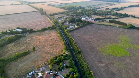 High-drone-shot-following-a-blue-train-making-its-way-through-British-countryside