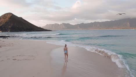 Young-blonde-woman-in-swimsuit-walking-on-beach-in-Hawaii,-slow-motion