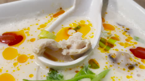 Authentic-and-delicious-Tom-Kha-Gai-Thai-with-chili-oil-and-herbs-in-white-bowl-and-large-spoon