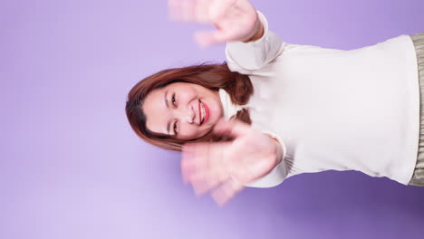 Vertikales-Porträt-Einer-Asiatischen-Glücklichen-Frau-Winkt-Der-Kamera-Zu-Und-Macht-Hallo-gesten,-Während-Sie-Isoliert-über-Einem-Violetten-Hintergrund-Steht