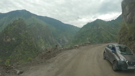 A-point-of-view-shot-of-a-vehicle-riding-through-dangerous-and-damaged-dirt-road-carved-through-steep-rocky-cliff-in-the-Himalaya-after-the-landslide