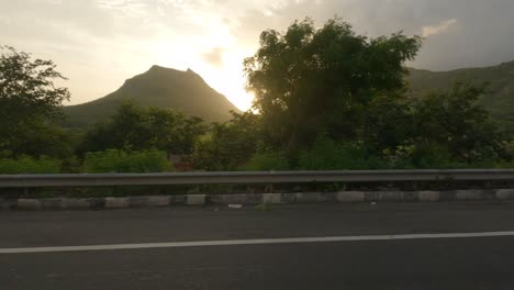 Side-view-of-a-car-driving-on-a-highway-in-Maharashtra-looking-at-the-beautiful-sunset-on-a-Sahyadri-mountain-landscape
