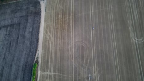 Aerial-footage-following-a-motorbike-driving-through-a-wheat-field,-with-a-contrasting-black-field-to-the-left
