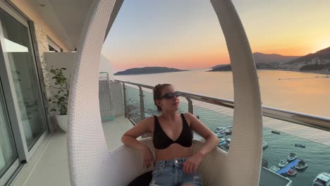 Junges-Mädchen,-Das-Während-Eines-Sonnenuntergangs-In-Einem-Schönen-Kleinen-Fischerdorf-In-Montenegro-Namens-Rafailovici-Für-Die-Kamera-Auf-Einem-Balkon-Posiert