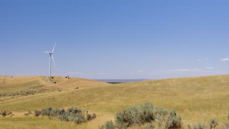 Wind-turbine-in-an-Idaho-field,-wide-with-farmland-and-sagebrush-hills-on-a-hot-summer-day-in-Eastern-Idaho-in-4K