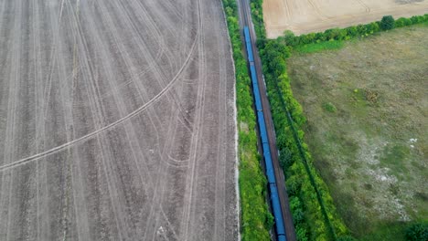 Drone-shot-of-a-blue-train-on-a-tree-lined-railway-going-through-British-countryside