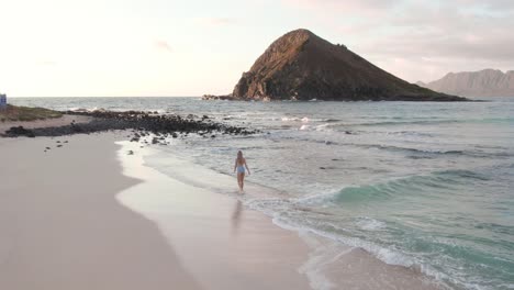 Young-woman-in-swimsuit-walking-on-beach-at-dusk,-Hawaii,-slow-motion