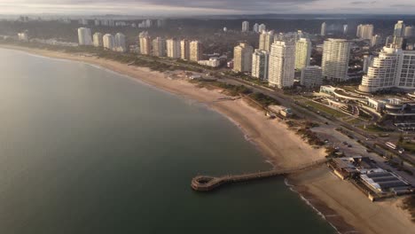 Aerial-view-over-sandy-beach-and-coast-of-Punta-del-Este-during-sunny-day-with-fog-in-air---BIg-buildings-with-ocean-view-in-Uruguay