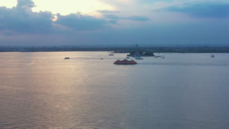 Aerial-rising-tilt-zoom-of-New-York-Harbor-with-the-Staten-Island-Ferry-and-the-Statue-of-Liberty-at-dramatic-sunset-dusk