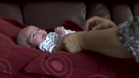 Calm-Adorable-Newborn-Baby-Looking-Whilst-Mother-Changes-His-Nappy-As-He-Lays-On-Sofa