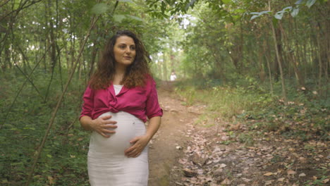 Pregnant-Woman-Expectant-Mother-Walking-Alone-in-Forest,-Attractive-Caucasian-Casual-Dressed-Mom-Stroking-Caressing-Touching-Her-Belly-with-Hands-Smiling,-Childbearing-Tenderness,-Medium-Portrait-Shot