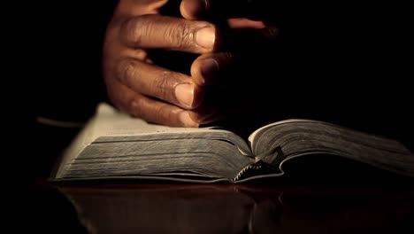 Rezando-Con-La-Mano-En-La-Biblia-Sobre-Fondo-Negro-Con-La-Gente-Metrajes