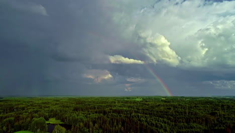 Aerial-view-over-forest-landscape-during-cloudy-day-with-rainbow-at-sky