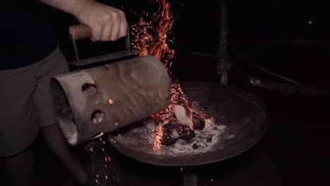 Man-empties-hot-charcoal-on-campsite-grill-with-red-embers-rising-up