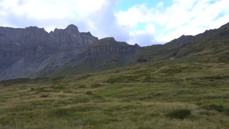 Wanderer-Zu-Fuß-Auf-Einem-Pfad-Zu-Einer-Berghütte-In-Einem-Weiten-Alpental,-Umgeben-Von-Felsigen-Gipfeln