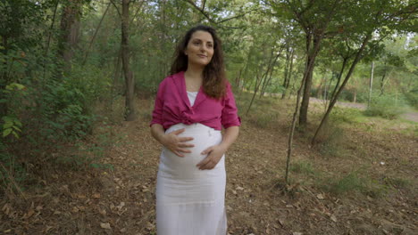 Pregnant-Woman-Expectant-Mother-Walking-Alone-in-Forest-Park,-Attractive-Caucasian-Casual-Dressed-Mom-Stroking-Caressing-Touching-Her-Belly-with-Hands-Smiling,-Childbearing-Love,-Medium-Portrait-Shot