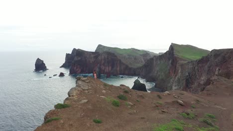 A-woman-is-standing-alone-in-a-pink-red-dress-in-the-wind-on-the-edge-of-a-cliff-in-Madeira