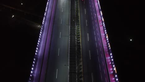 Video-De-Drones-De-Arriba-Hacia-Abajo-De-Un-Puente-En-La-Noche-Iluminado-Por-Luces-Led-Violetas