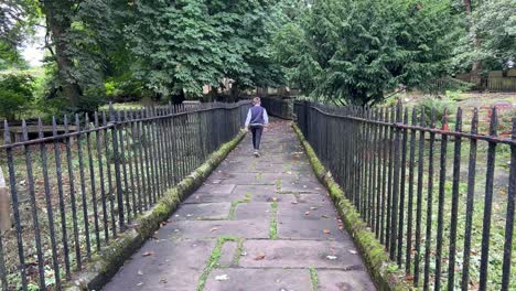 Young-Boy-walking-through-the-graveyard-at-St-Michael-and-All-Angels-Church-Graveyard,-Haworth,-final-resting-place-of-the-Bronte-family